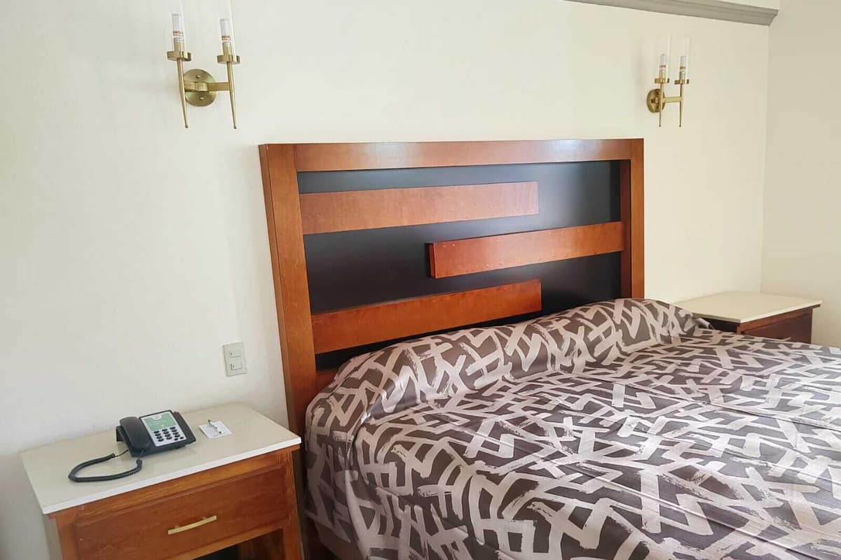 A bedroom with a wooden headboard, a patterned bedspread, a bedside phone, and a nightstand.