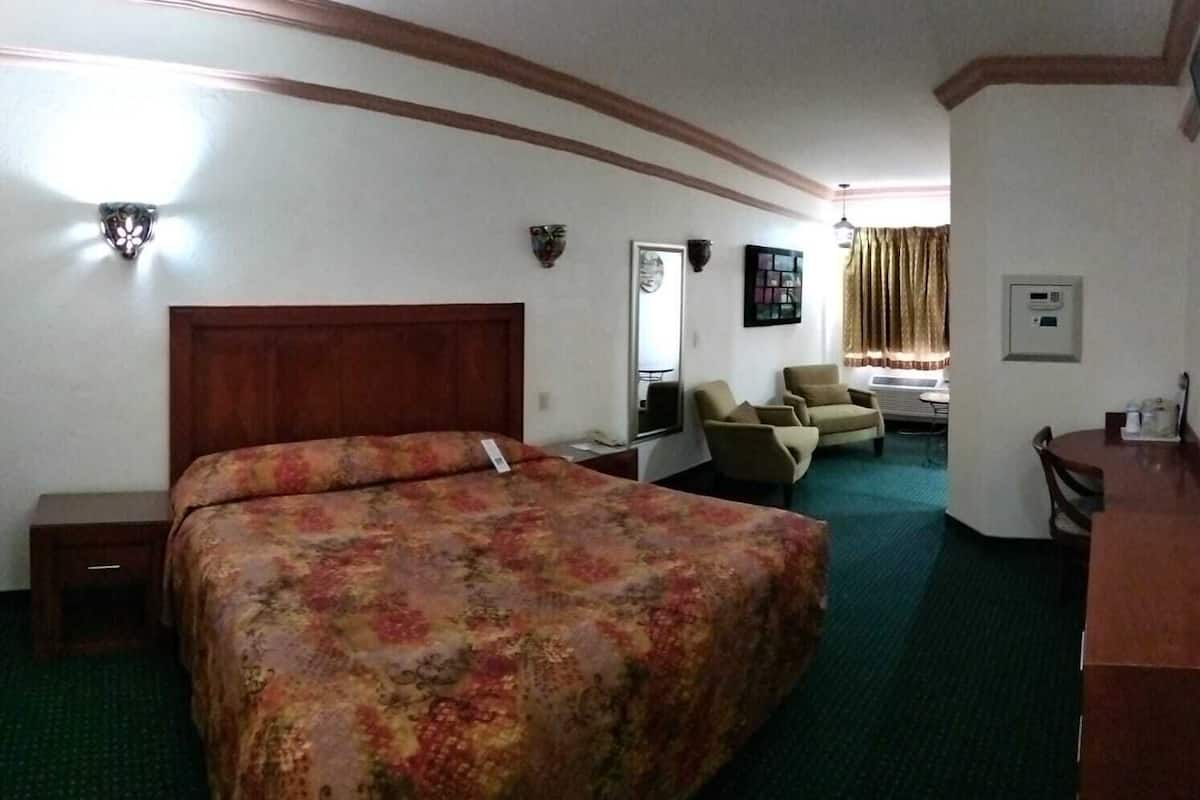 A hotel room with a large bed, a desk, a chair, and a small table.
