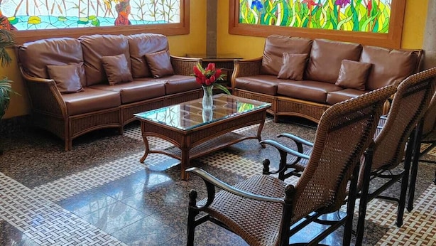 Habitació amb sofà, taula de cafeteria, cadires de vimetla i dues finestres amb vitralls de motius florals.