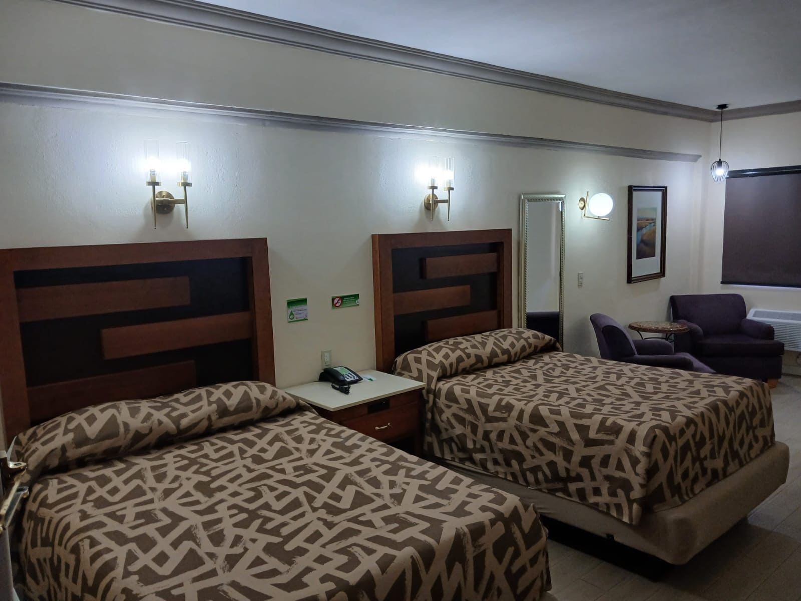 Une chambre d’hôtel avec deux lits, un bureau avec un téléphone, une chaise, un miroir et une fenêtre donnant sur un paysage agréable.