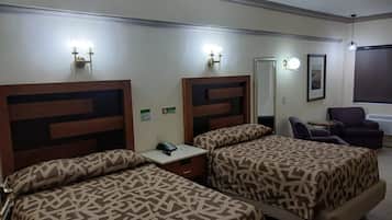 Une chambre d’hôtel avec deux lits, un bureau avec un téléphone, une chaise, un miroir et une fenêtre donnant sur un paysage agréable.