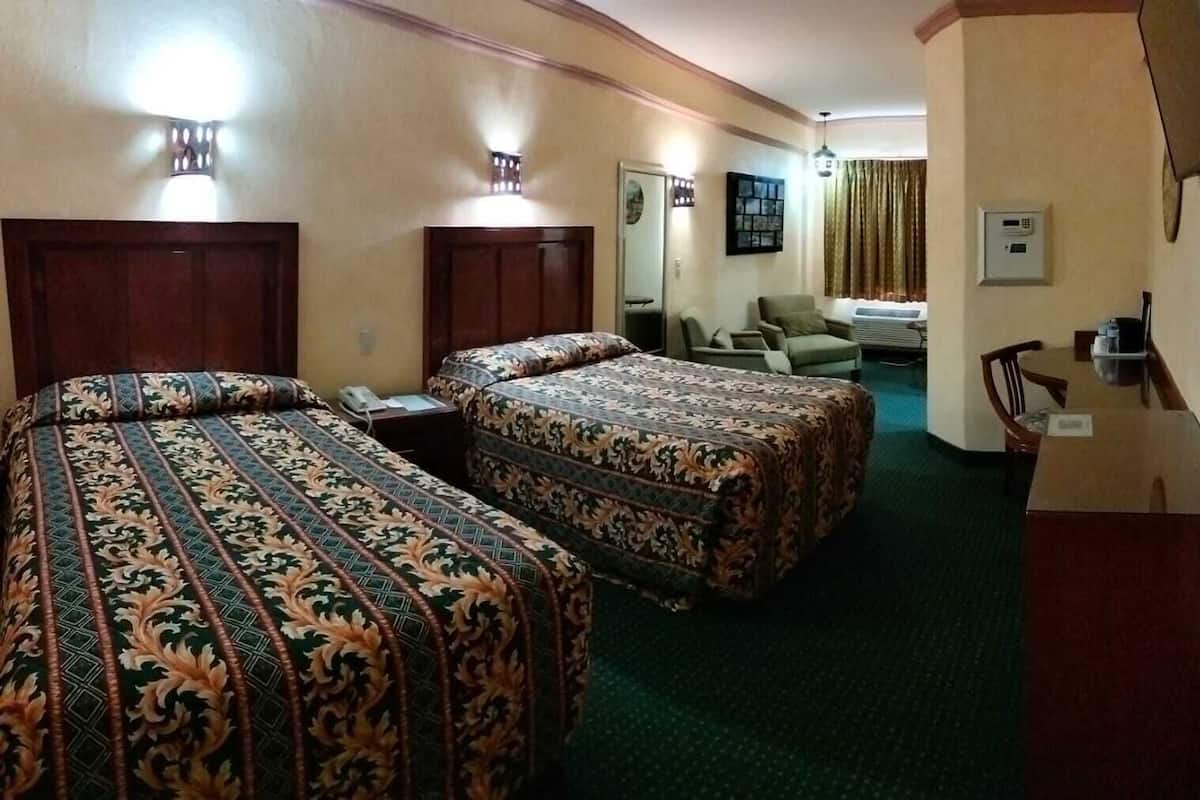 A hotel room with two beds, a desk, a chair, a dining table, and a window with curtains.