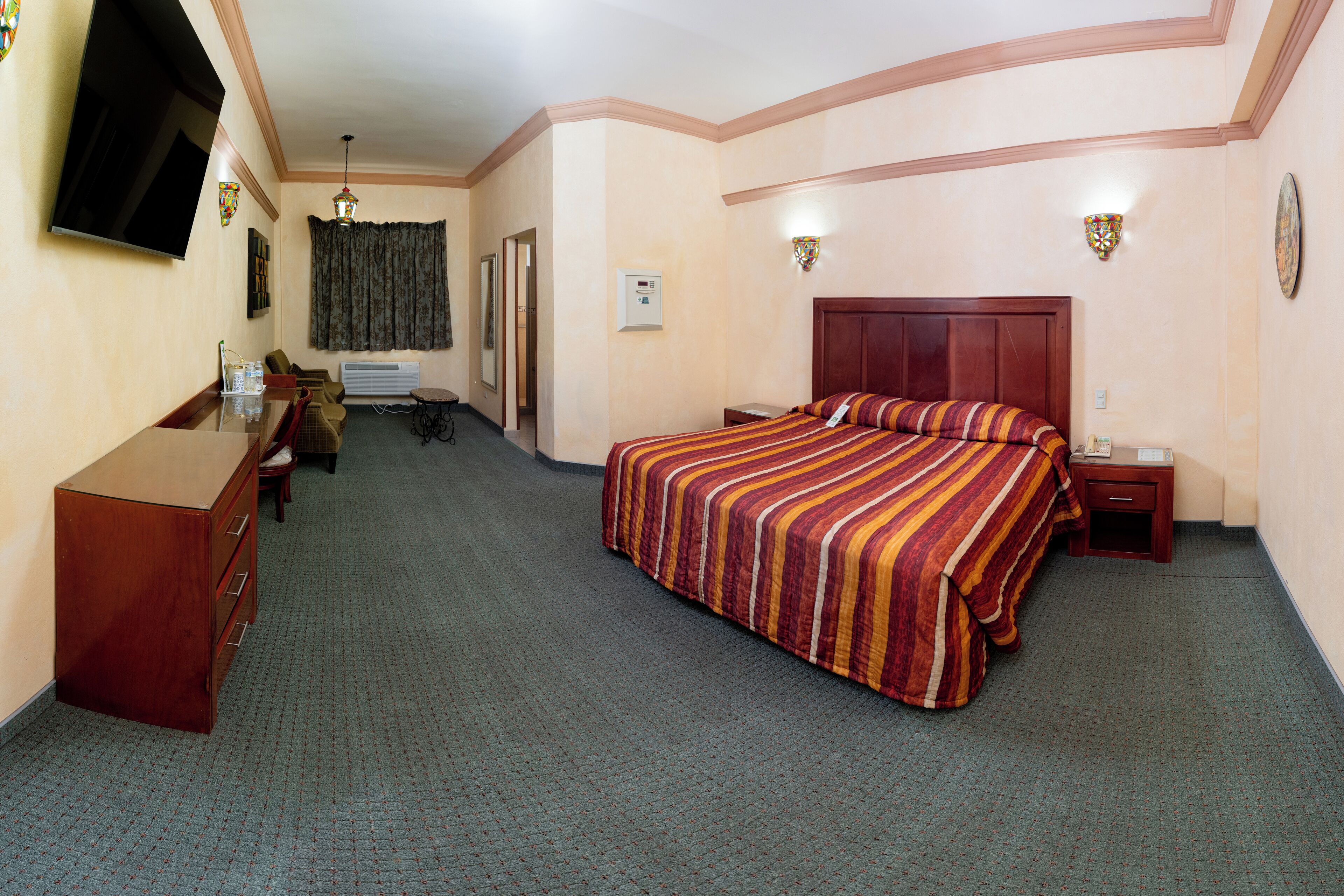 Quarto de hotel com cama, escrivaninha, cômoda, televisão e janela com cortinas.