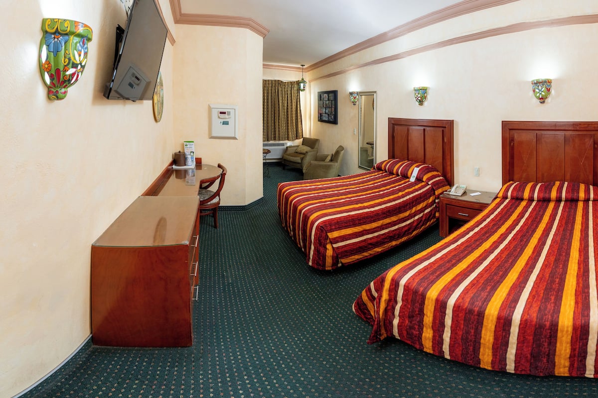 A hotel room with two beds, a desk, a chair, a television, and a bathroom.