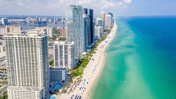 Un paisaje urbano costero con rascacielos, una playa y un mar azul cristalino.