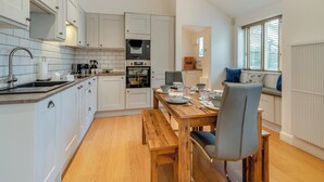 Une cuisine moderne avec des meubles blancs, une table à manger en bois et une fenêtre équipée de stores.