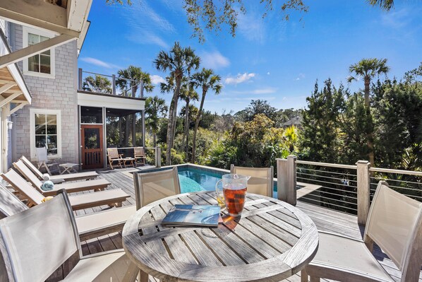 Zona de piscina con sillas de descanso, una mesa y una bebida.