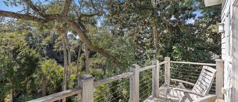 A wooden deck with a railing, overlooking a lush garden and trees.