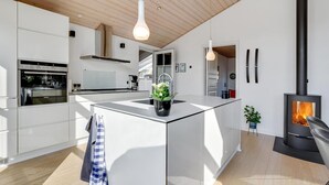 A modern kitchen with a central island, stainless steel appliances, and a wood-burning stove. - Awesome home in Broager (Broager)