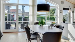 A modern kitchen with large windows, a dining table with chairs, and a hanging light fixture. - Awesome home in Broager (Broager)