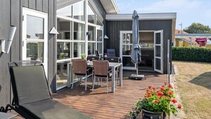 A modern outdoor patio with a wooden deck, a dining area with chairs and a table, and a large umbrella. - Awesome home in Broager (Broager)