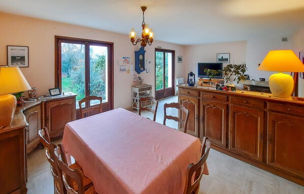 A dining area with a table set for four, wooden cabinets, a chandelier, and a television on a stand. - 4 bedroom beach front home in Plougasnou (Plougasnou)