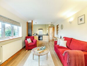 A cozy living room with a red sofa, a red armchair, and a coffee table. There is a kitchen in the background with a stove and cabinets.
