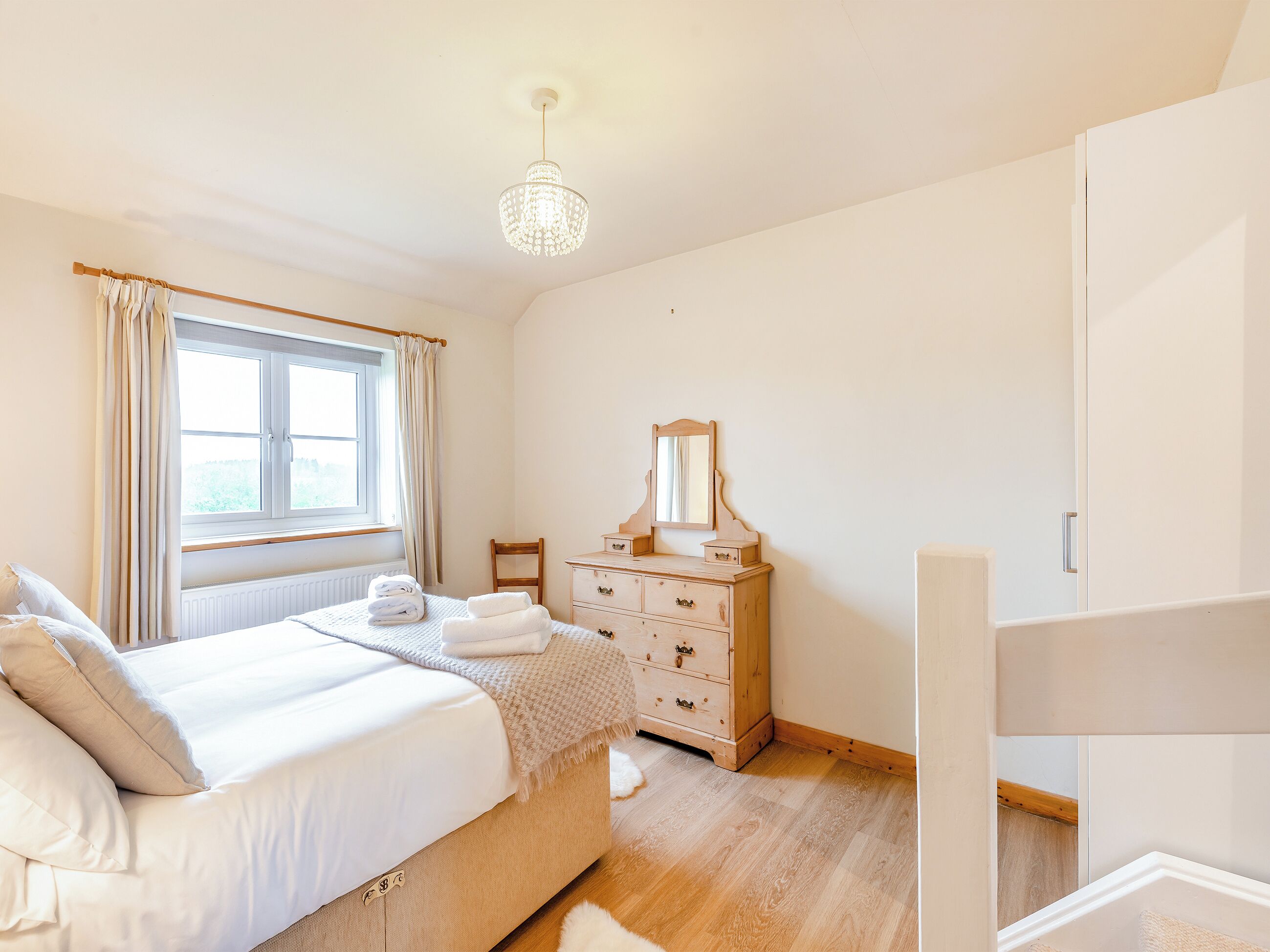 Ein Schlafzimmer mit Bett, Schminktisch, Spiegel und einem Fenster mit Vorhängen.