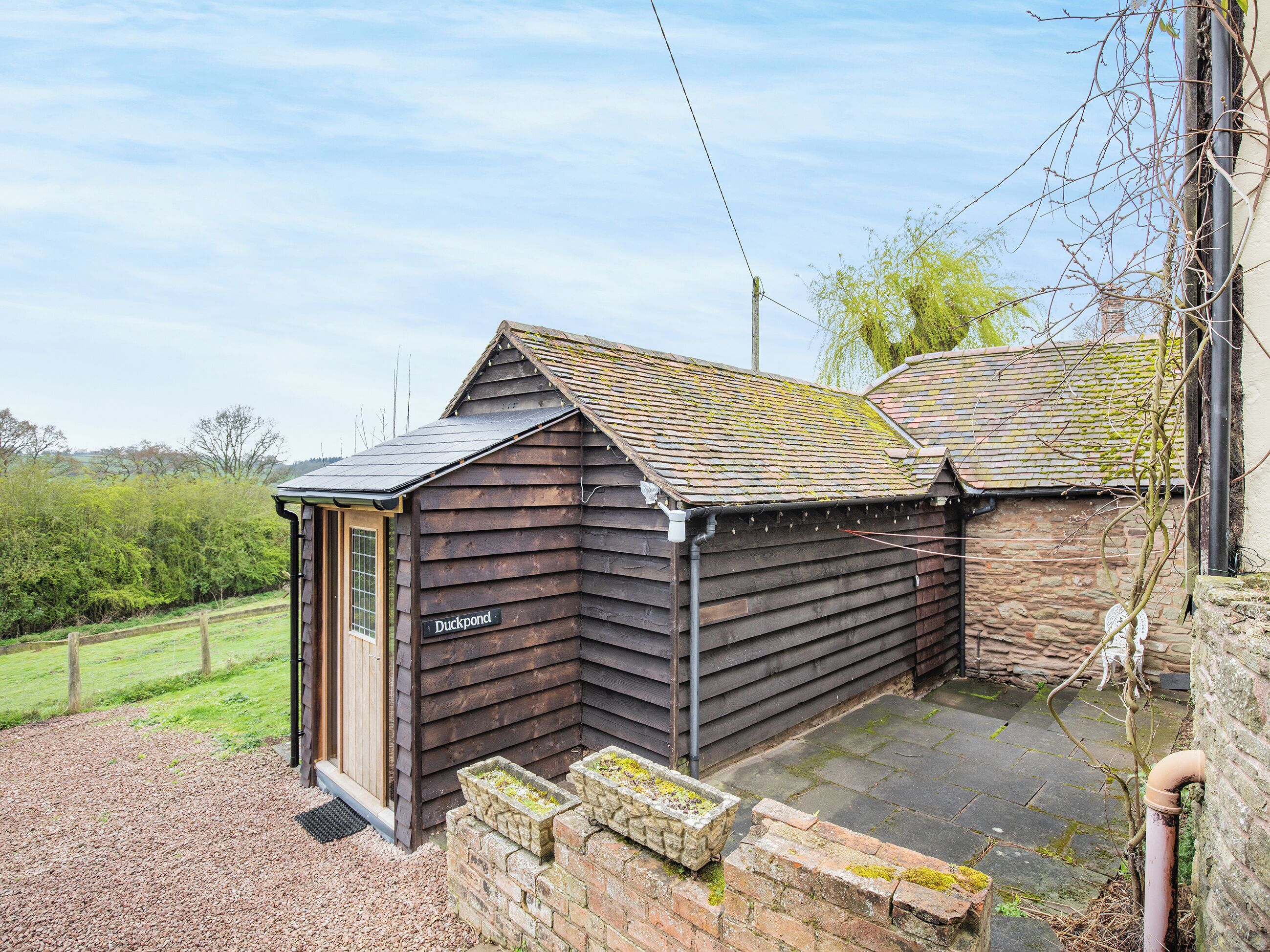 A small wooden building labeled "Duckpond" with a sloped roof, a brick foundation, and a gravel path leading to it.