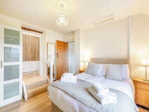 A bedroom with a bed, two bedside lamps, a wooden headboard, a nightstand, and a staircase leading to another room.