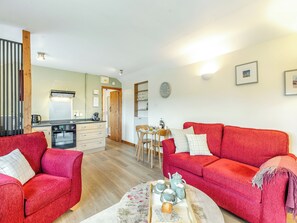 A cozy living room with a red sofa, a wooden coffee table with tea sets, and a kitchen in the background.