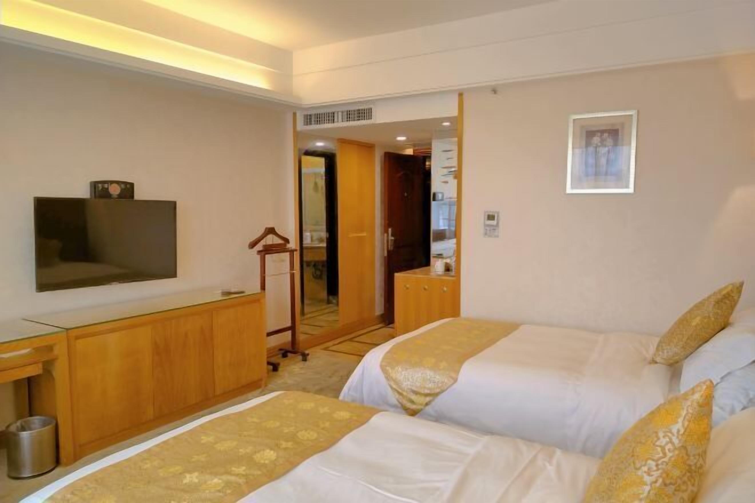 A hotel room with two beds, a TV, a wooden desk, and a mirror.