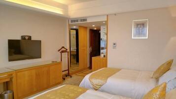 A hotel room with two beds, a TV, a wooden desk, and a mirror.