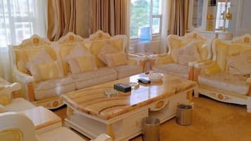 A luxurious living room with ornate sofas, a marble coffee table, and a large window with curtains.