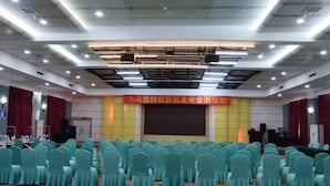 A conference room with rows of teal chairs and a stage with a red banner. - Jinjiacheng Hotel (Shantou)