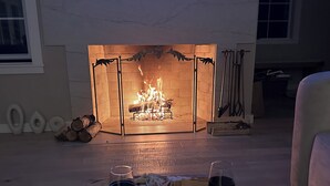 A cozy room with a fireplace, a wooden table with cheese and wine glasses, and a couch.