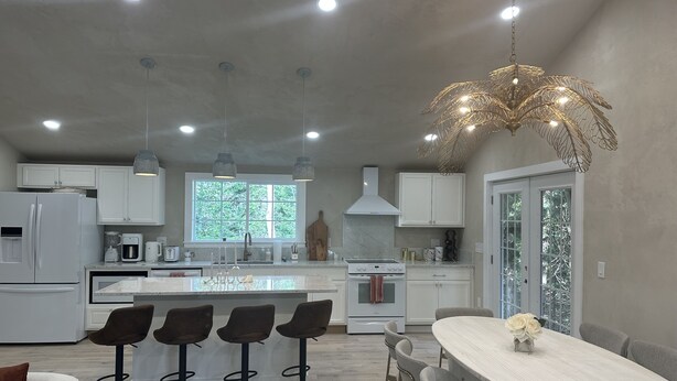 A modern kitchen with white cabinets, a central island, bar stools, and a dining table.