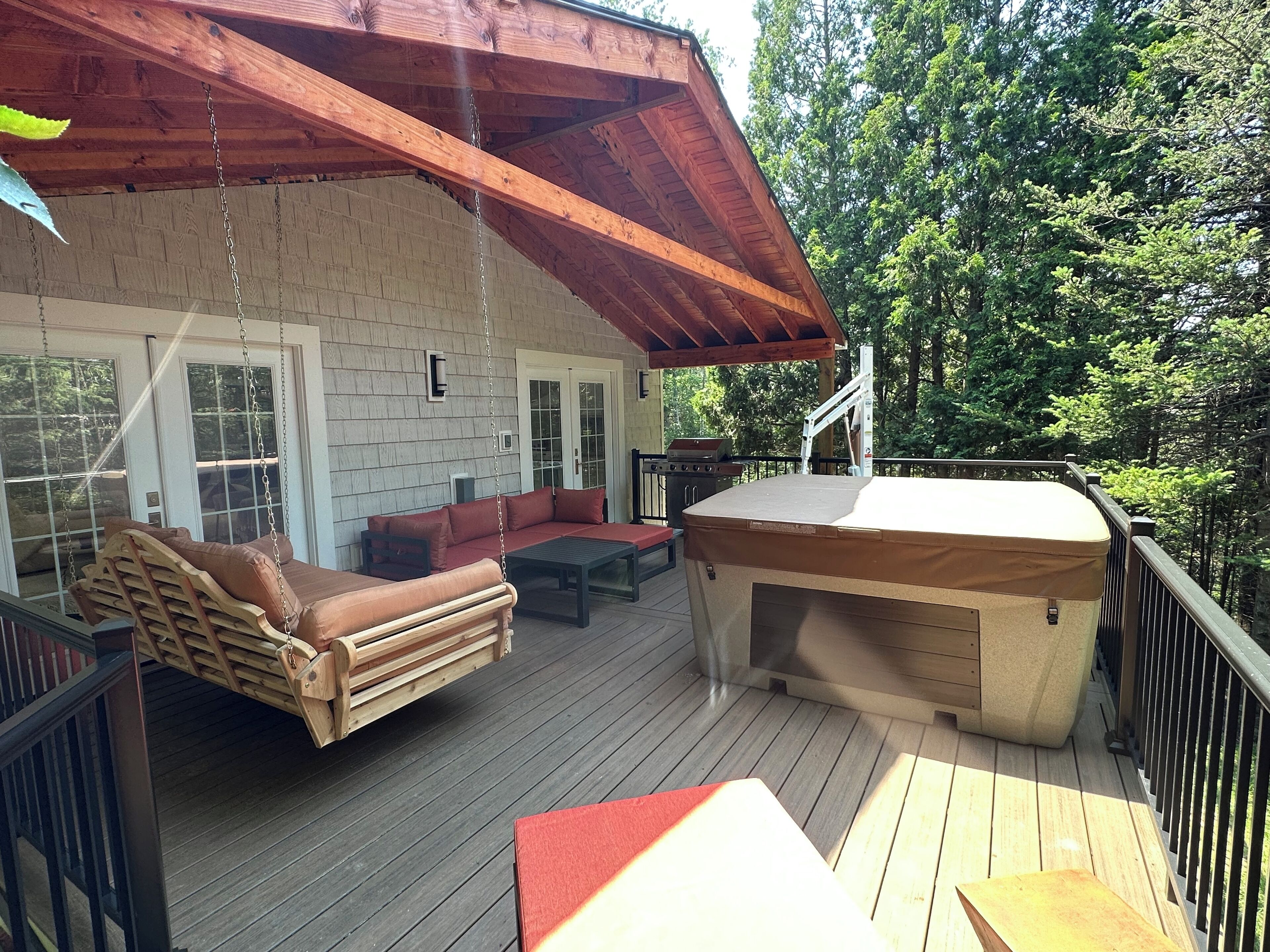 A covered deck with a wooden bench, a sofa, and a hot tub.