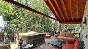 A covered outdoor deck with a grill, seating area, and a view of the forest.