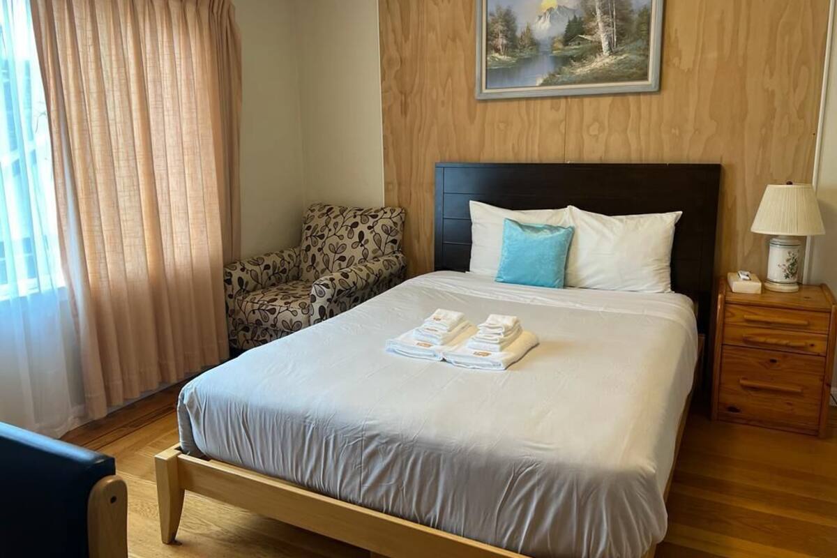 A neatly made bed with a blue pillow, a wooden nightstand with a lamp, and a painting on the wall.