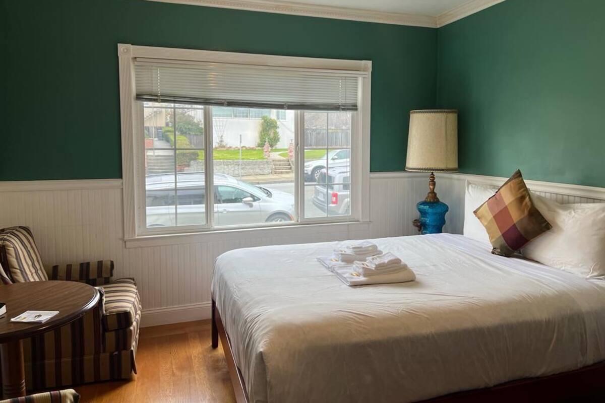 A hotel room with a large bed, a window with blinds, a lamp, and a chair.