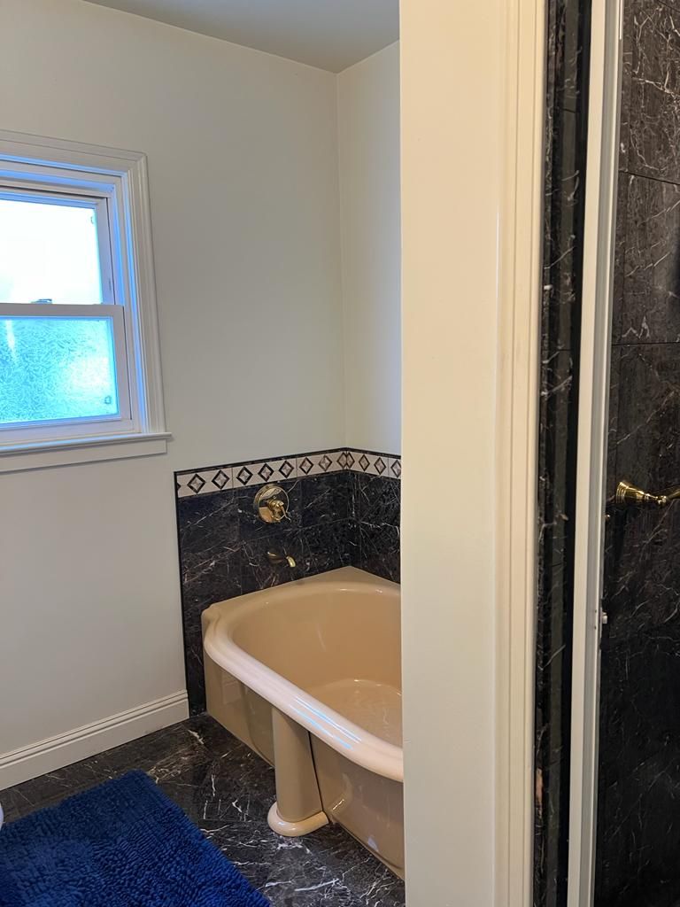 A bathroom with a bathtub, a window, and a blue bath mat.