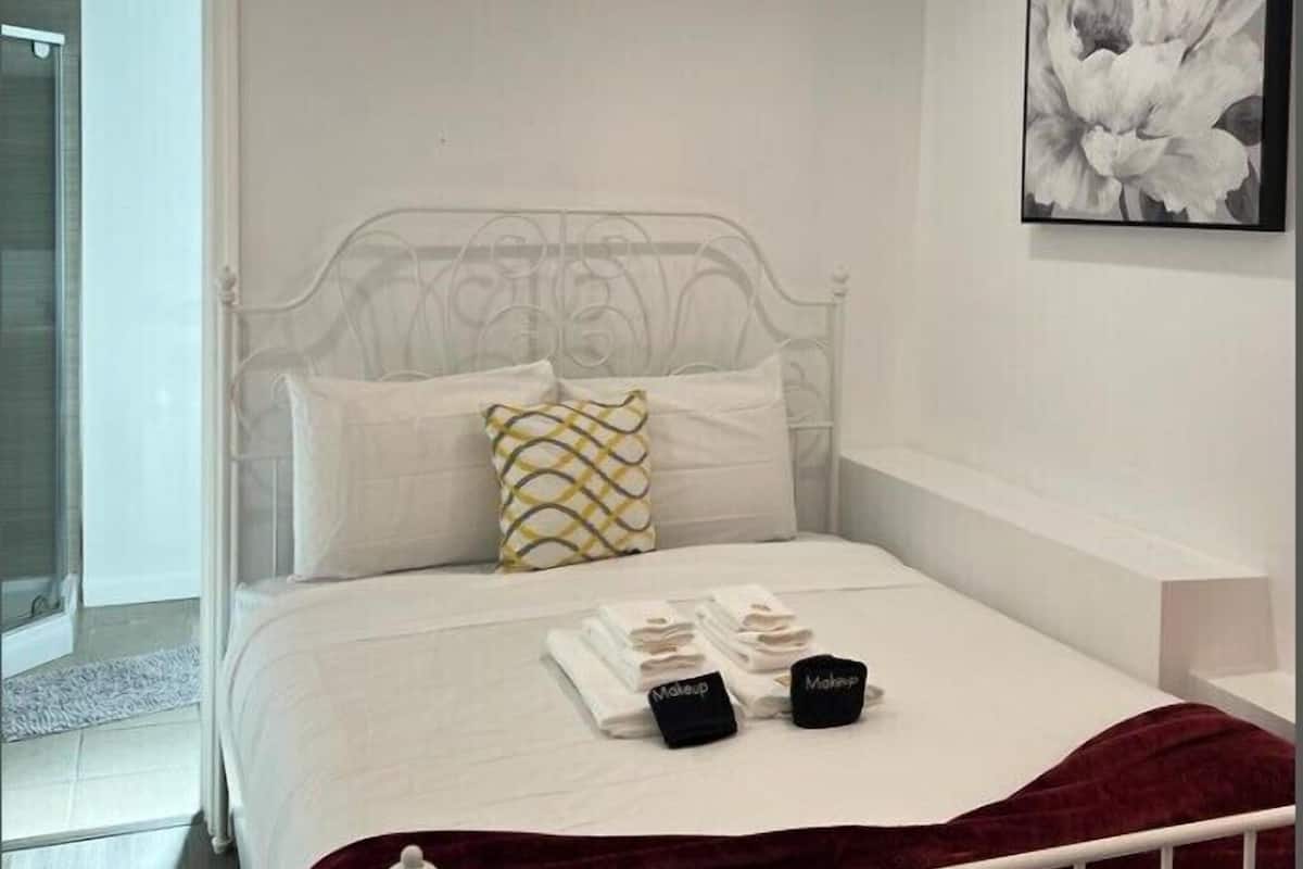 A bedroom with a white bed, a red throw blanket, and a framed floral artwork on the wall.
