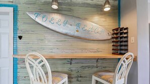 A surfboard with "Folly Beach" written on it, two white chairs with patterned cushions, and a wooden shelf with storage bins. - Boogie Down! Classic Folly Vibe, Lower level unit. (Folly Beach)