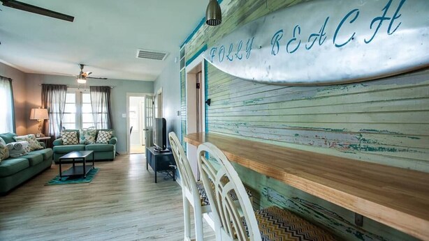 A living room with a green sofa, a white chair, a small table, and a TV. - Boogie Down! Classic Folly Vibe, Lower level unit. (Folly Beach)