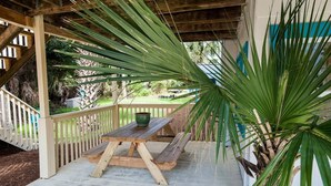 A covered patio with a wooden table and benches, surrounded by lush greenery and a view of a residential area. - Boogie Down! Classic Folly Vibe, Lower level unit. (Folly Beach)
