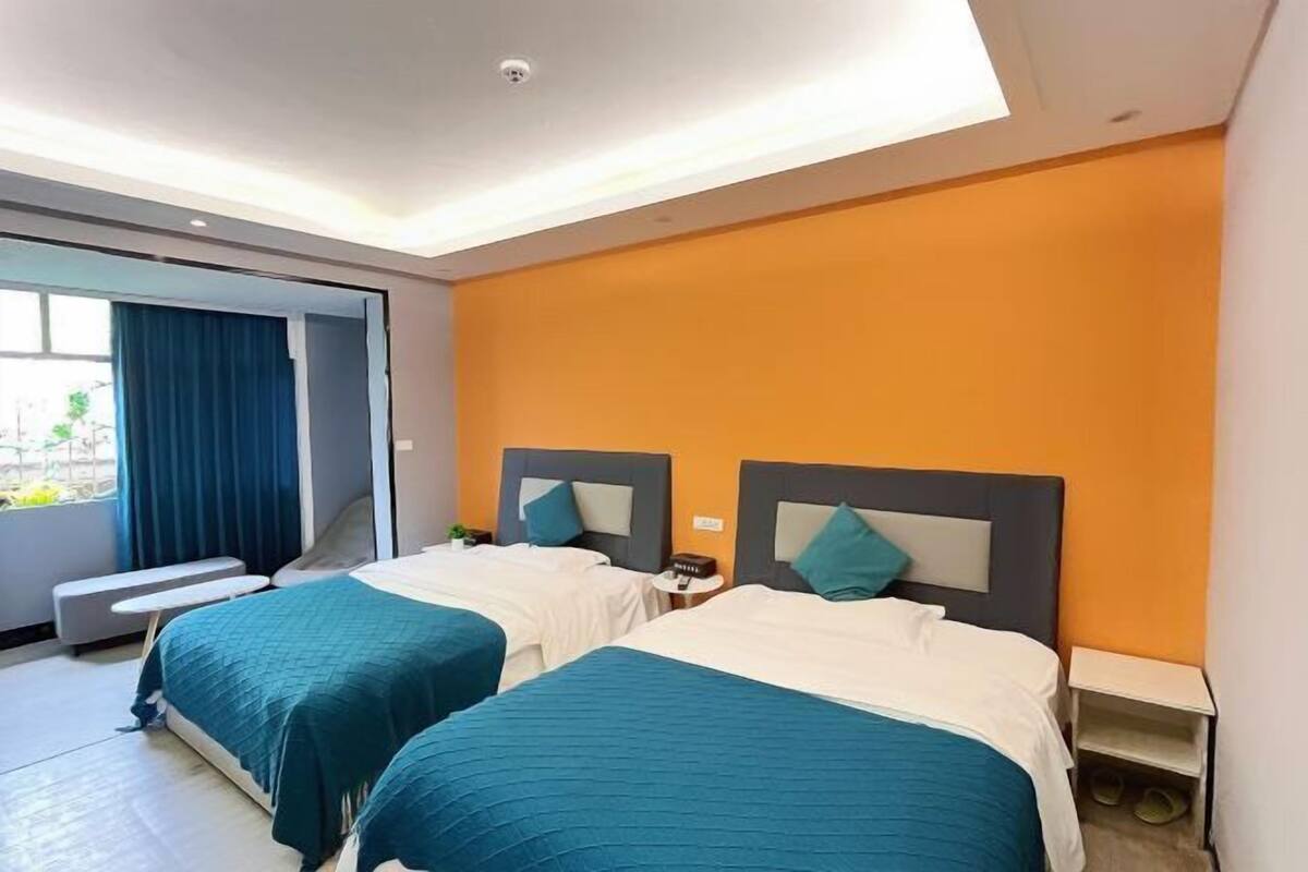 Habitación de hotel con dos camas, un banco, una mesita pequeña y una mesita de noche.