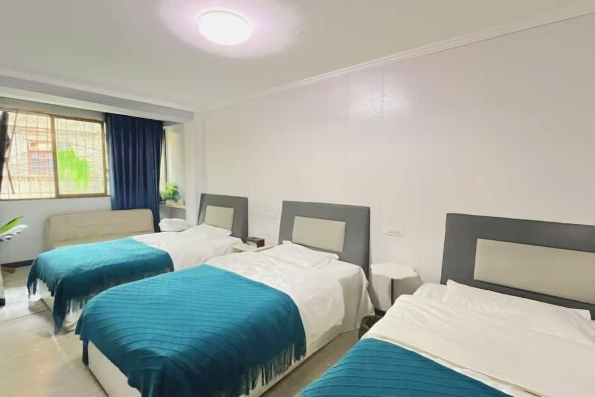 Habitación de hotel con tres camas, una ventana con cortinas, una mesita de noche y una lámpara en el techo.