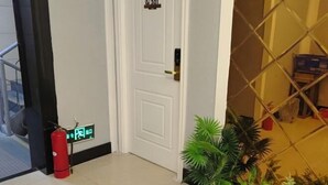 Entrada de hotel con extintor, una puerta con placa de número y una planta en maceta.