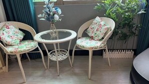 Una habitación con dos sillas de mimbre con cojines estampados, una mesita redonda pequeña y un jarrón con flores.