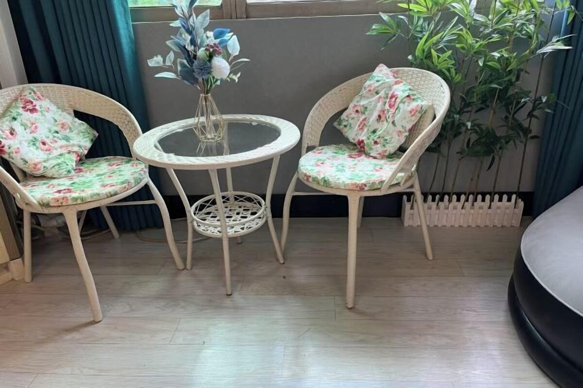 Ein Zimmer mit zwei Korbstühlen, floralen Kissen, einem kleinen runden Tisch und einer Vase mit Blumen.