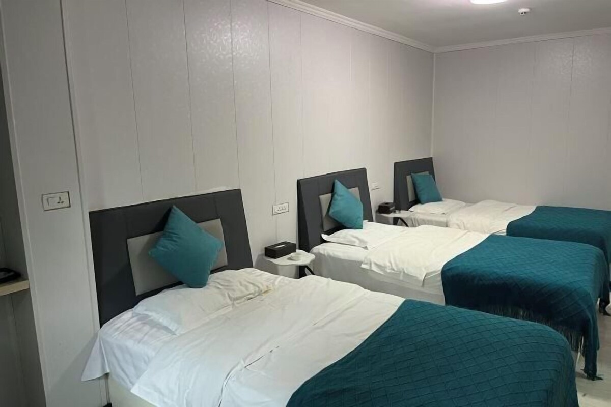 Ein Hotelzimmer mit drei Einzelbetten, jedes mit einer türkisblauen Bettdecke und passenden Kissen.