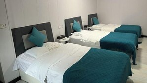 Habitación de hotel con tres camas, cada una con cubrecama color turquesa y ropa de cama blanca.