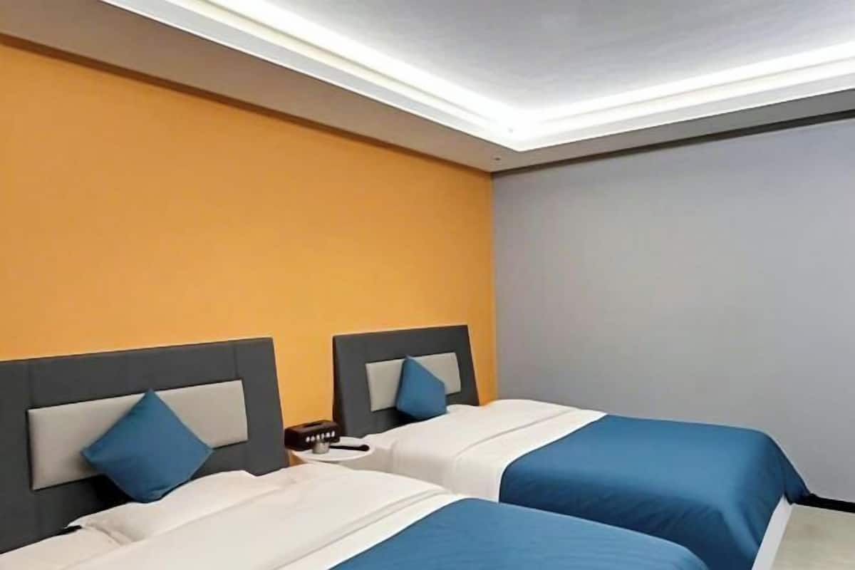 Habitación de hotel con dos camas, una mesita de noche y un aplique en el techo.