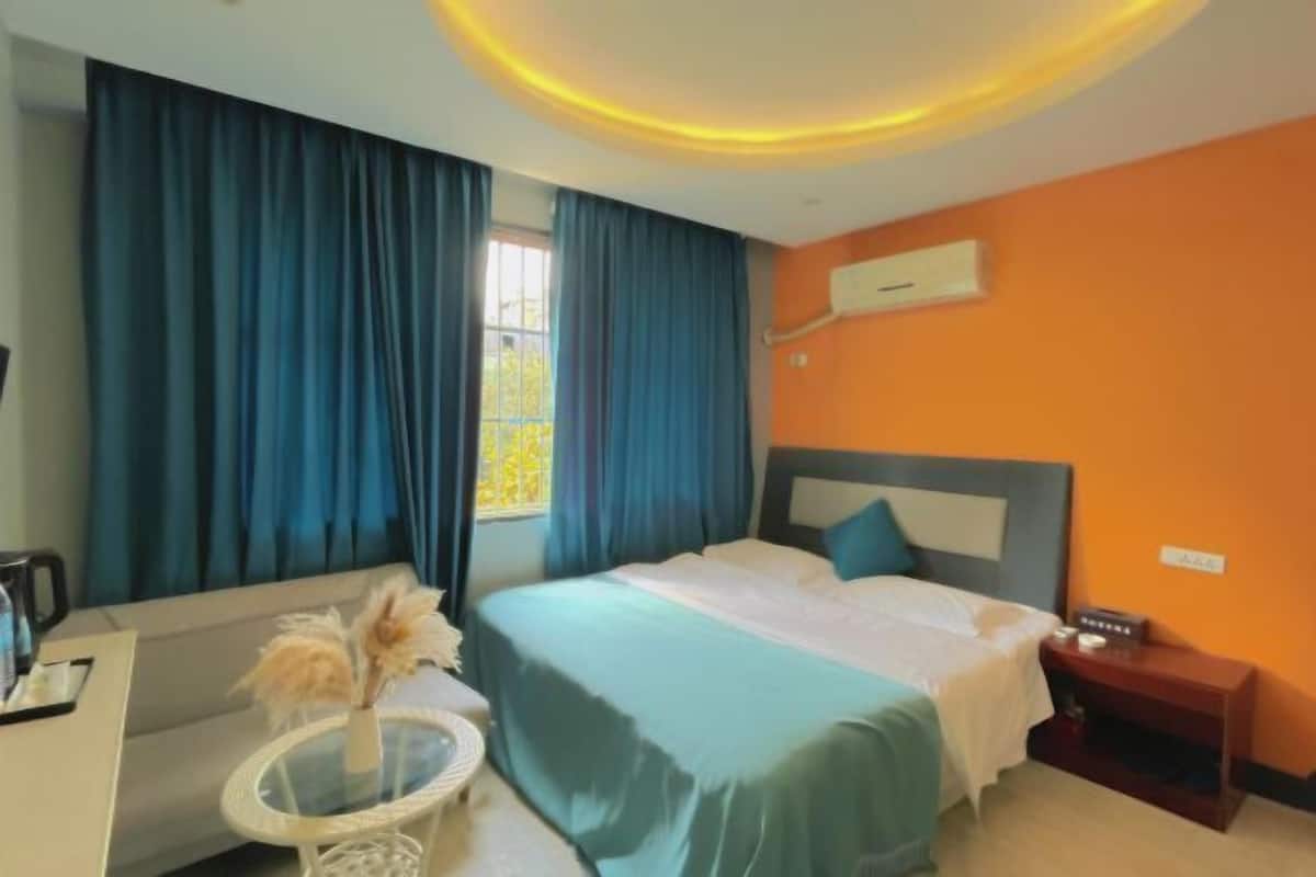 Habitación de hotel con cama, escritorio, silla, una mesita con un florero y ventana con cortinas.