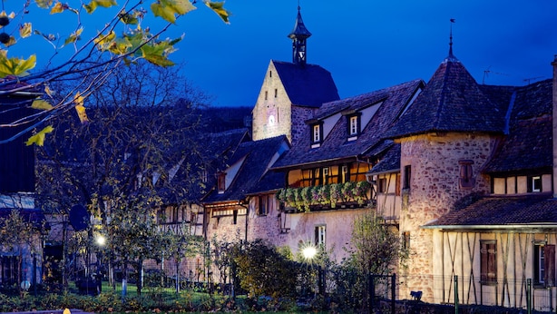 Een typisch Europees dorp met stenen gebouwen, een opvallende kerktoren en een verzorgde tuin.