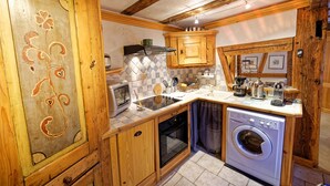 Een keuken met houten kastjes, een magnetron, een spoelbak, een vaatwasser en een betegelde achterwand.