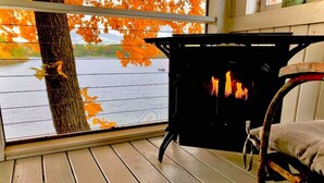 Eine Holzterrasse mit Kamin, einem Stuhl und Blick auf einen See mit Herbstlaub.