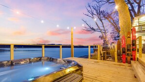 Eine Holzterrasse mit Whirlpool, einem Holenzaun und Blick auf das Wasser.