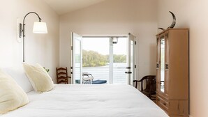 Ein Schlafzimmer mit einem großen Bett, einer Holzkommode und Seeblick durch eine geöffnete Tür.